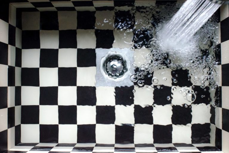 Shower head spraying water into a black and white tiled bathtub